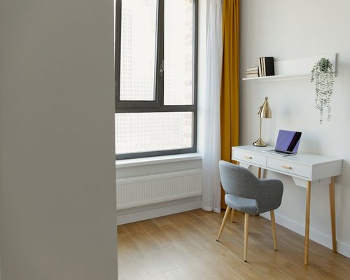 A modern workspace with a laptop on a wooden desk near a large window in a bright apartment