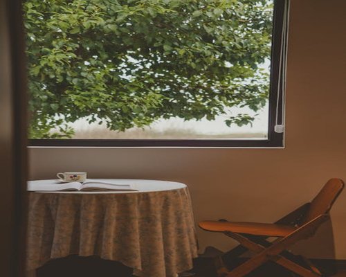 A well lit reading nook by a large window showing green trees outside, with an open book and a cup of tea