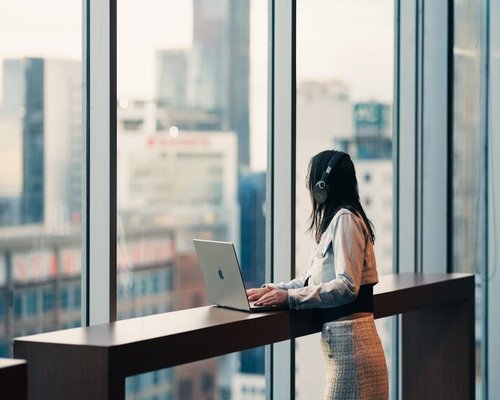 A professional looking away from their laptop and staring out the window at the city view